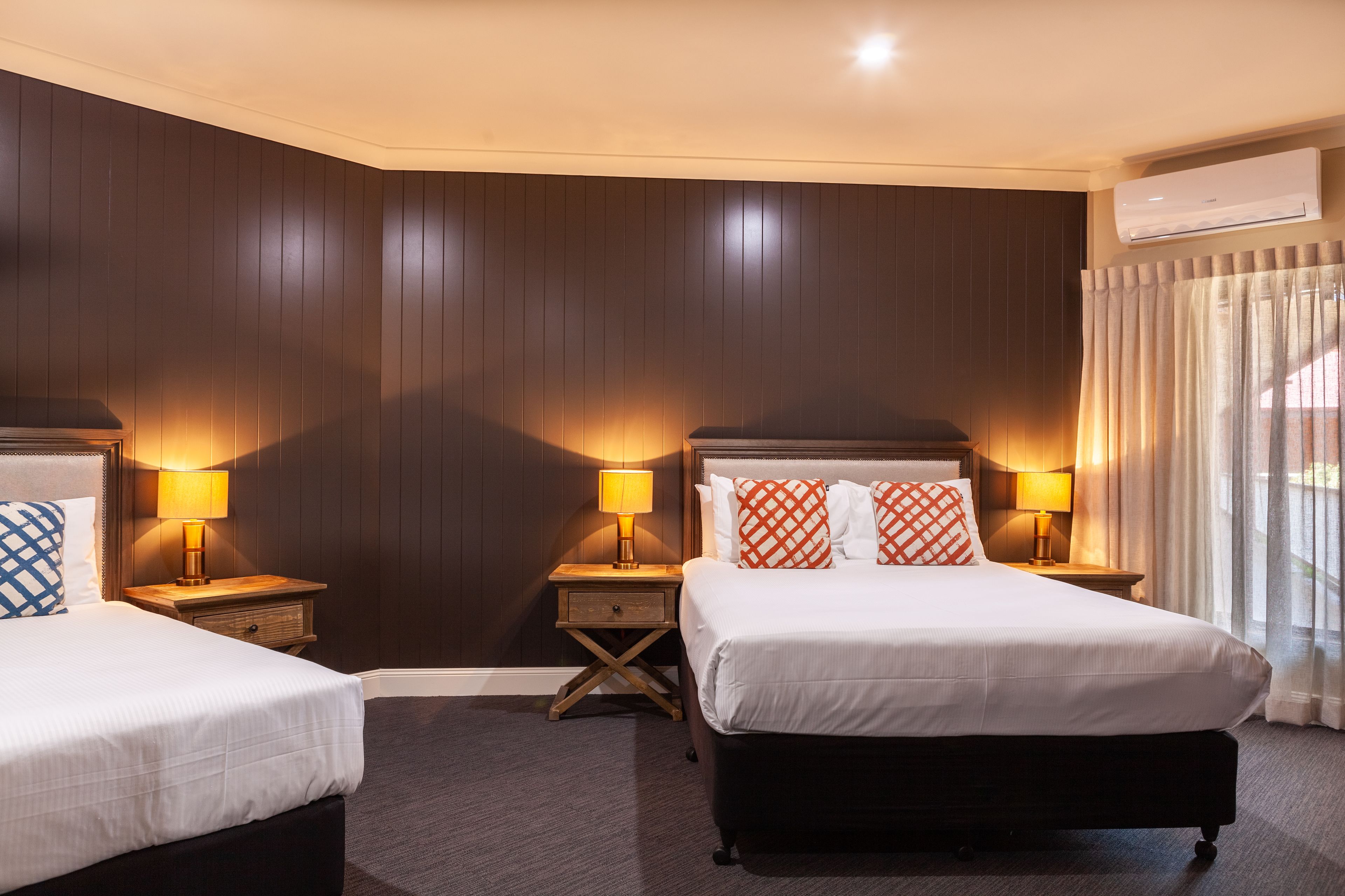 Een hotelkamer met twee bedden, houten paneelwanden en een airconditioning.