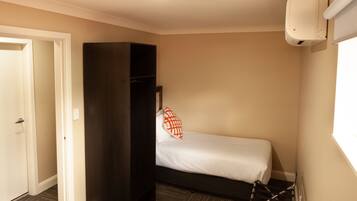 A small, single-bed room with a dark wardrobe, a white wall-mounted air conditioner, and a window providing natural light.