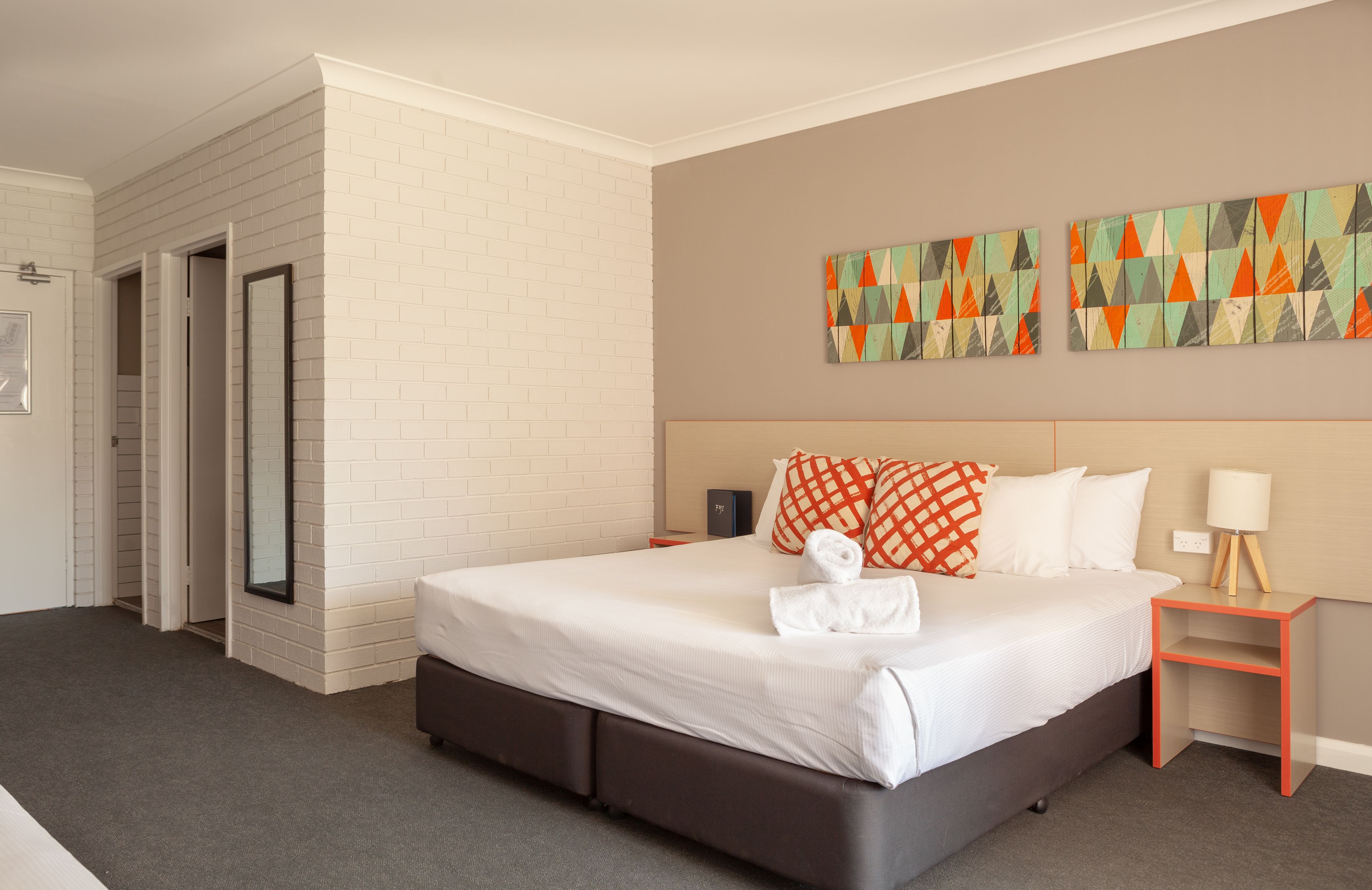 A hotel room with a large bed, a bedside table, a nightstand, and a wall with colorful artwork.