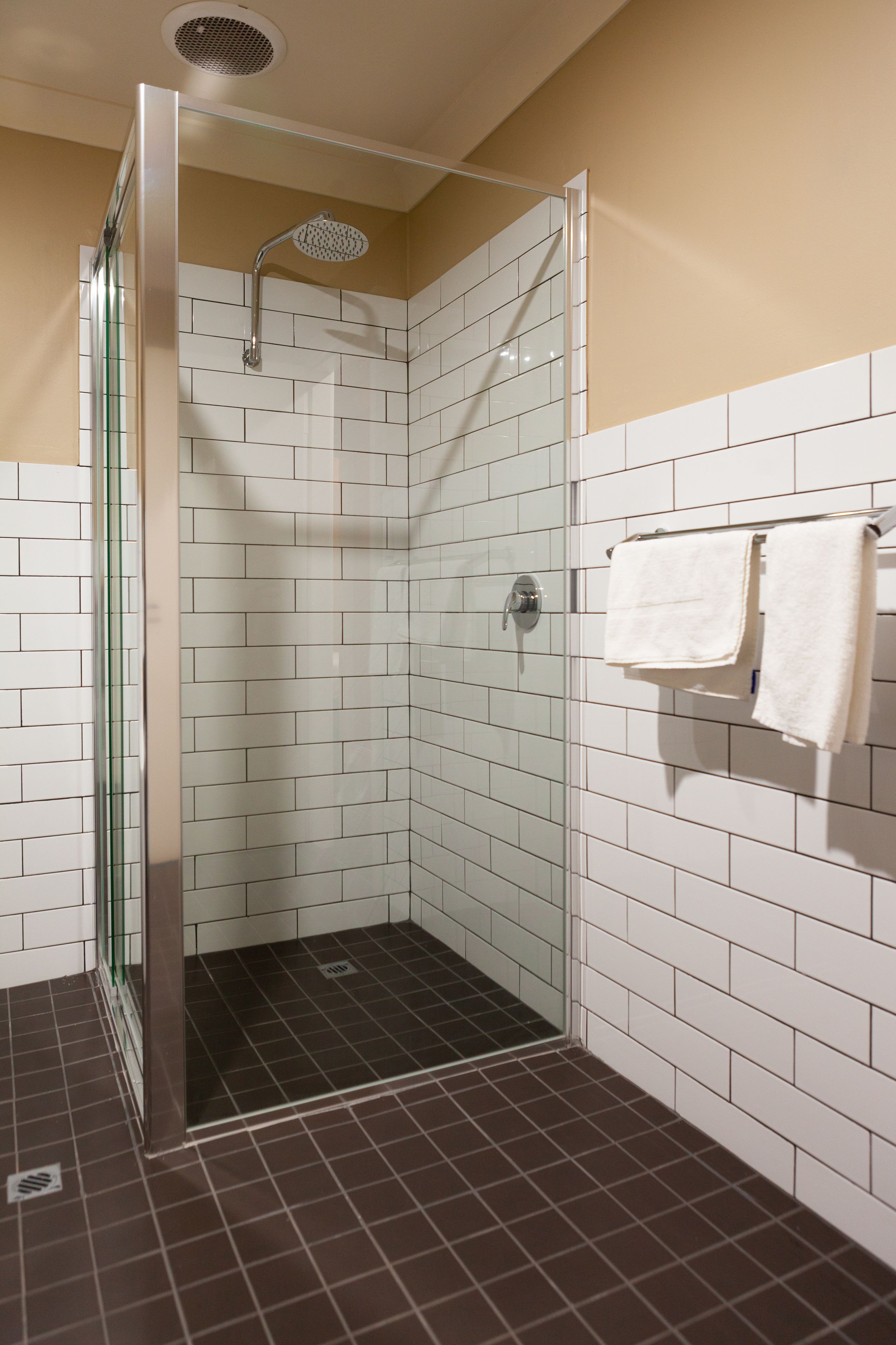 A shower with a glass door, white tiled walls, and a brown floor.
