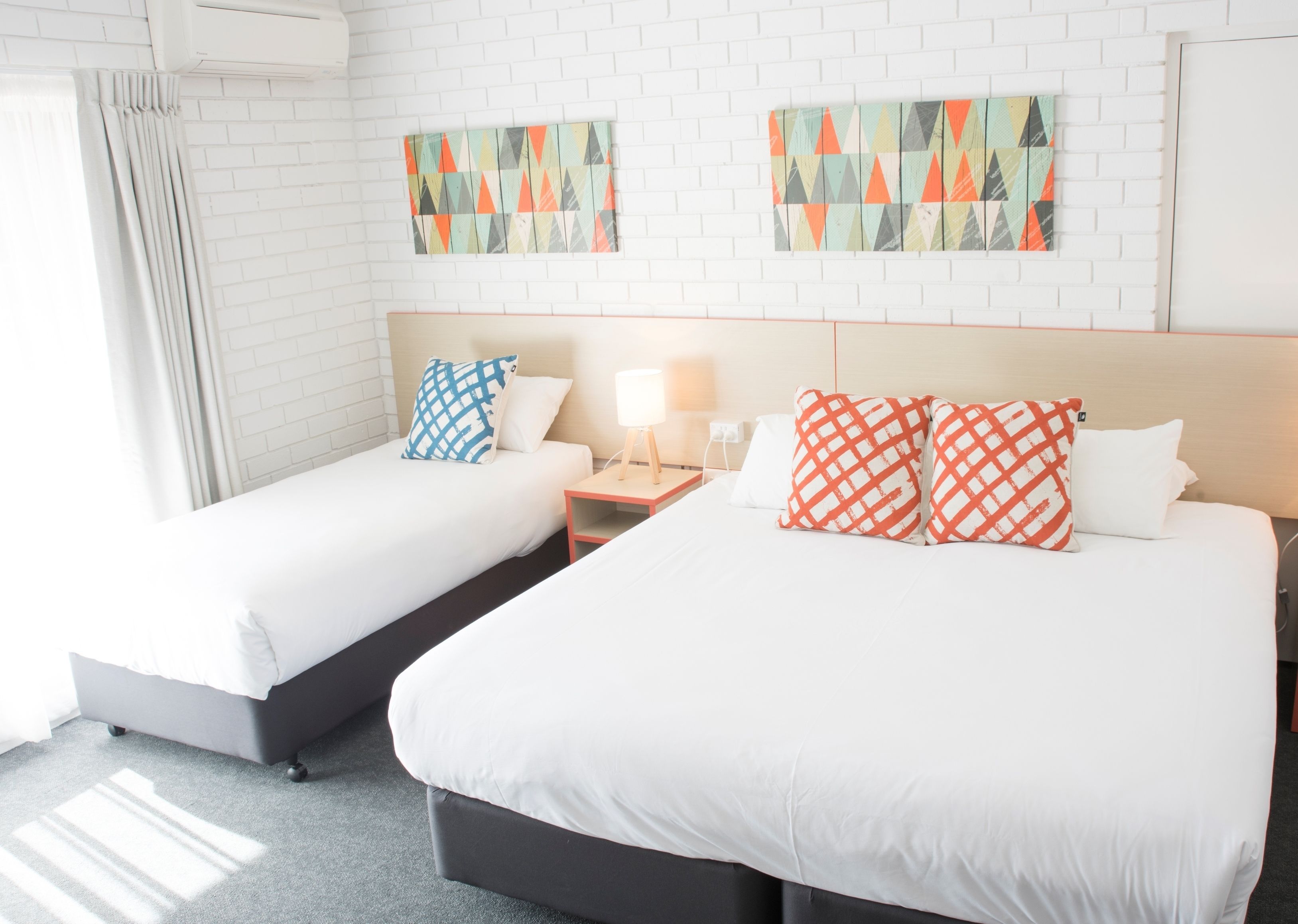 Een hotelkamer met twee bedden, witte beddengoed, een nachtkastje met een lamp en twee kunstwerken aan de muur.