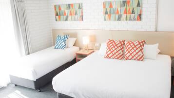 Een hotelkamer met twee bedden, witte beddengoed, een nachtkastje met een lamp en twee kunstwerken aan de muur.