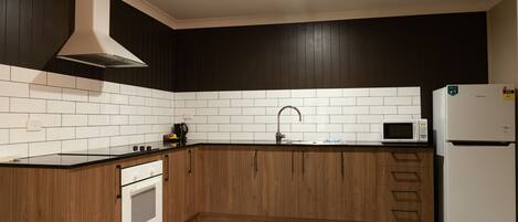 A kitchen with dark wooden cabinets, white subway tiles, a stainless steel range hood, a microwave, and a refrigerator.