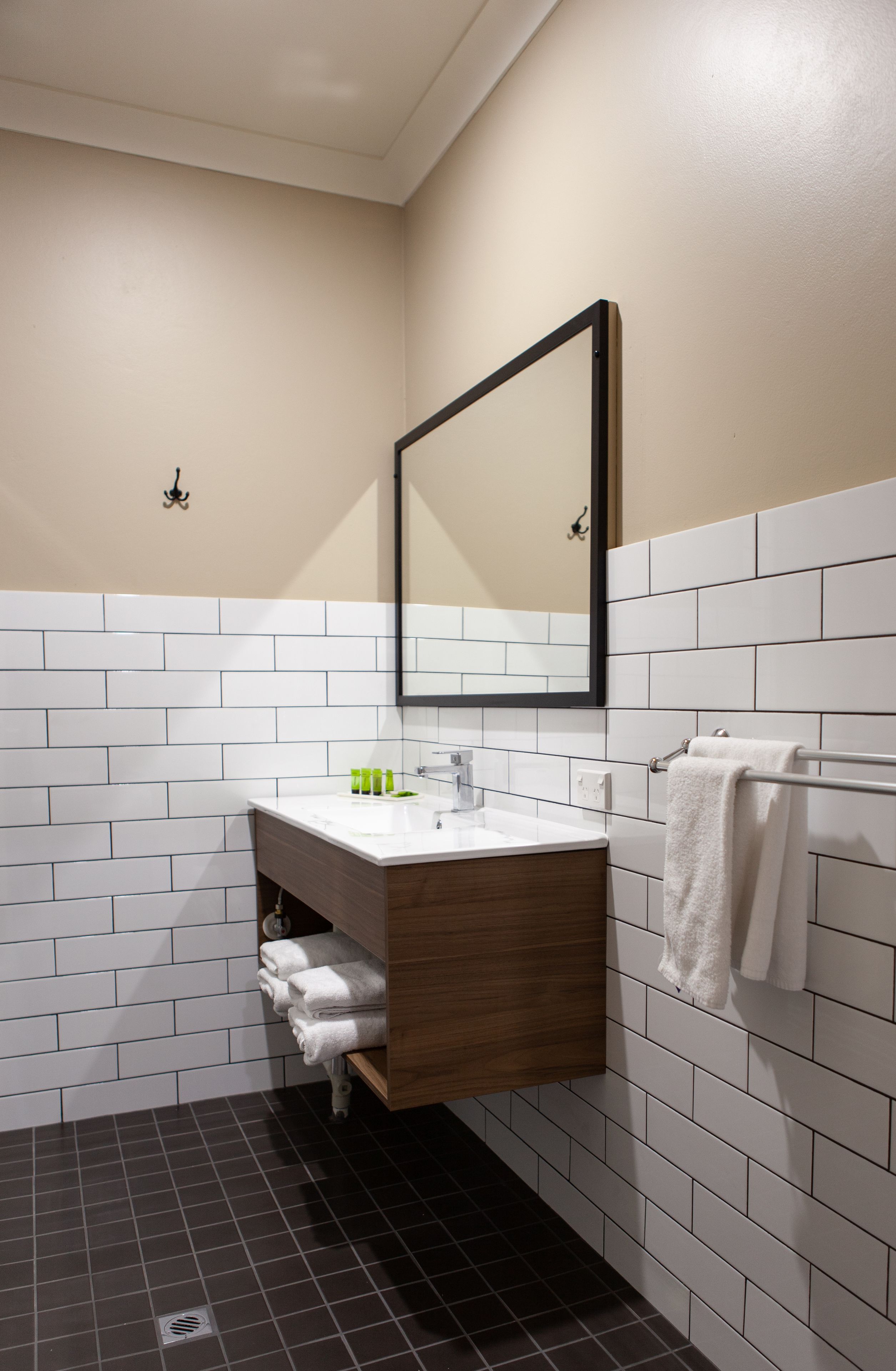 A modern bathroom with white subway tiles, a wooden vanity, a mirror, and a towel rack.