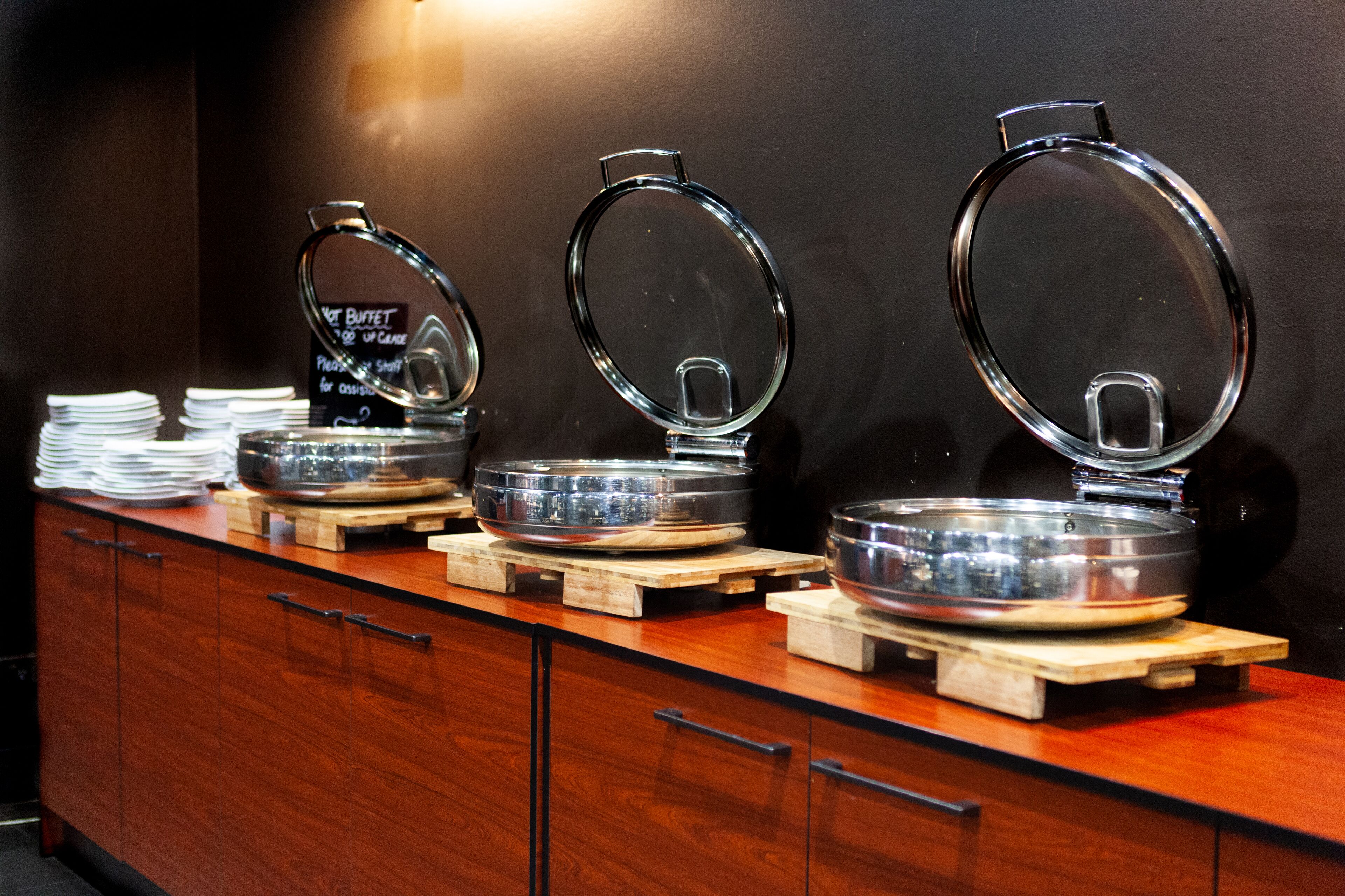 A buffet setup with multiple serving stations, each with a glass lid and a metal bowl.
