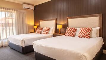 Two double beds with white linens and red and white checkered pillows, a wooden headboard, a nightstand with a lamp, and an air conditioning unit on the wall.