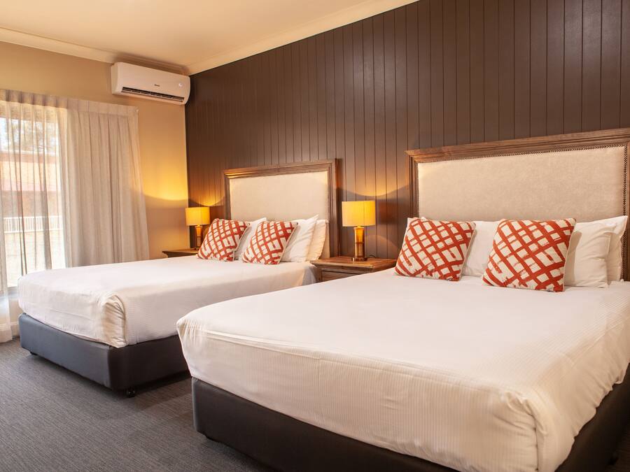 Two double beds with white linens and red and white checkered pillows, a wooden headboard, a nightstand with a lamp, and an air conditioning unit on the wall.