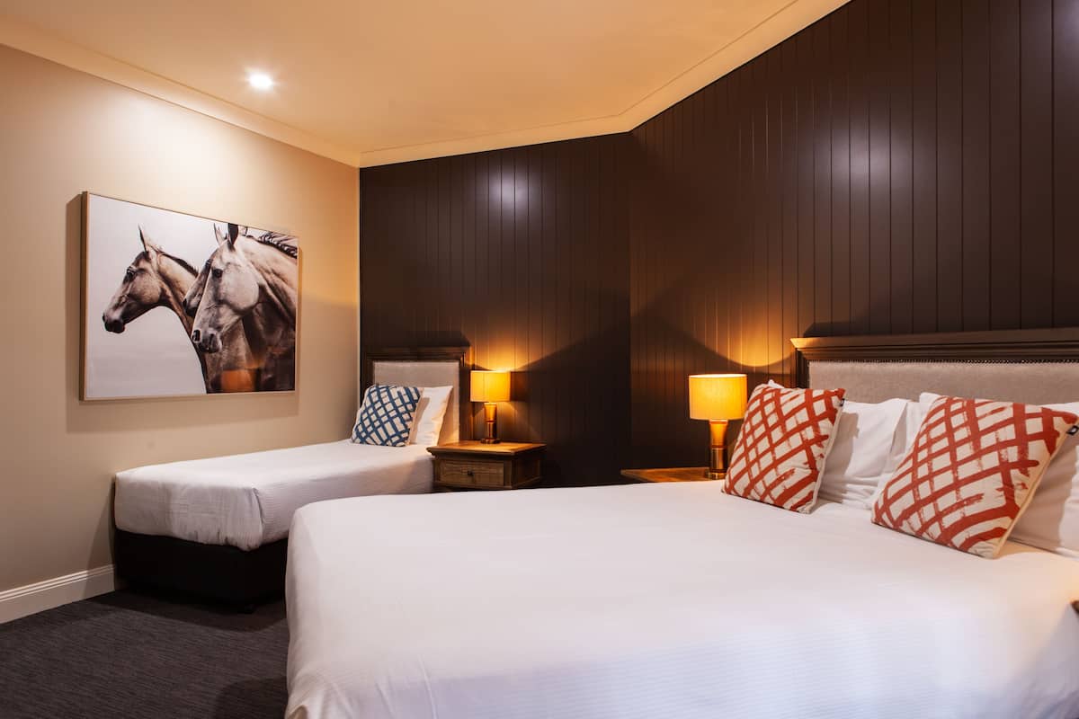 Ett hotellrum med två separata sängar, ett stort väggmonterat konstverk som föreställer hästar och träpanel på väggarna.