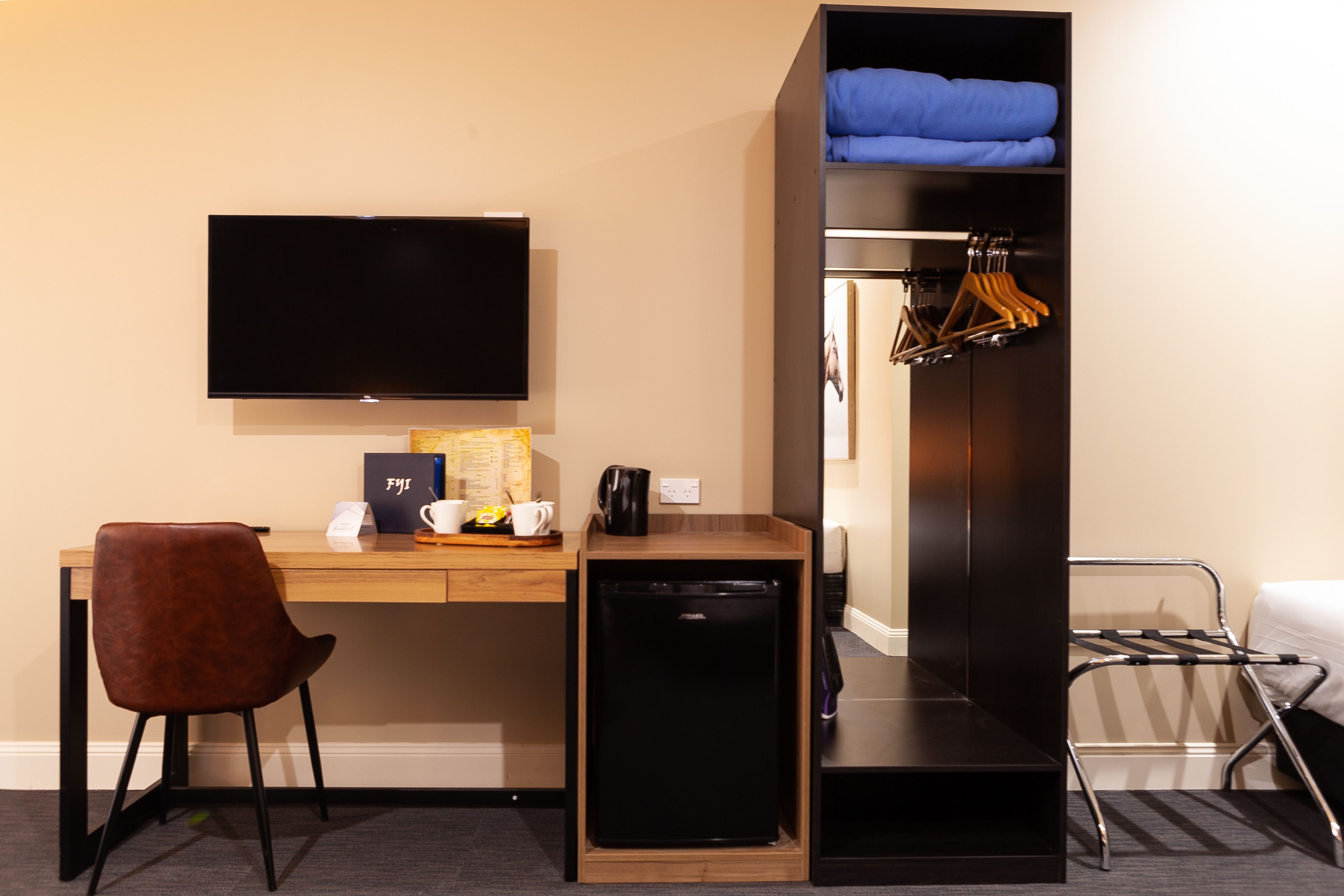Une chambre d’hôtel de taille réduite, équipée d’un bureau, d’une télévision, d’un petit réfrigérateur, d’une chaise, d’une armoire et d’un lit.