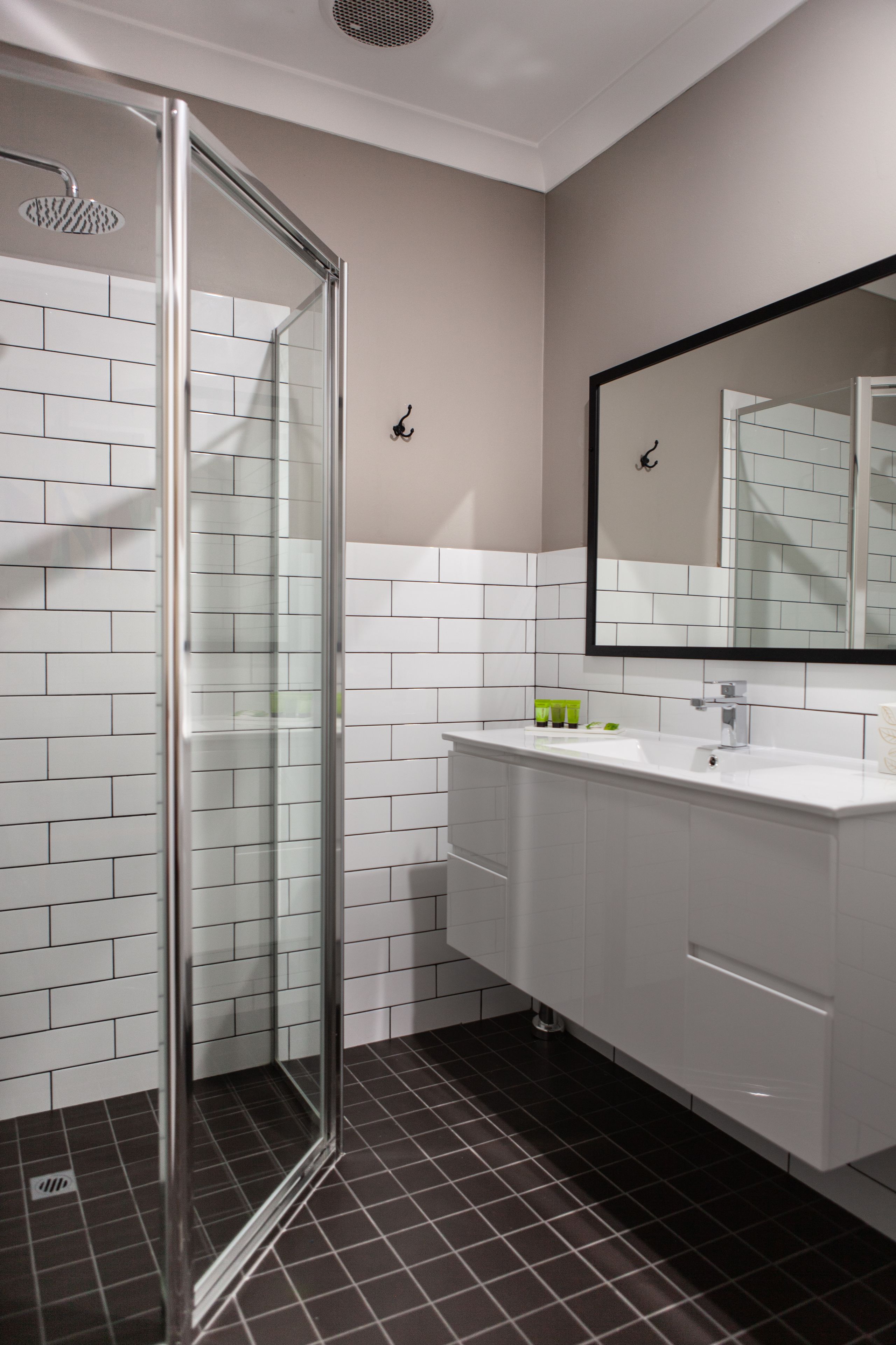 Een moderne badkamer met een glazen douchecabine, witte betegelde wanden en een grote spiegel boven de wastafel.