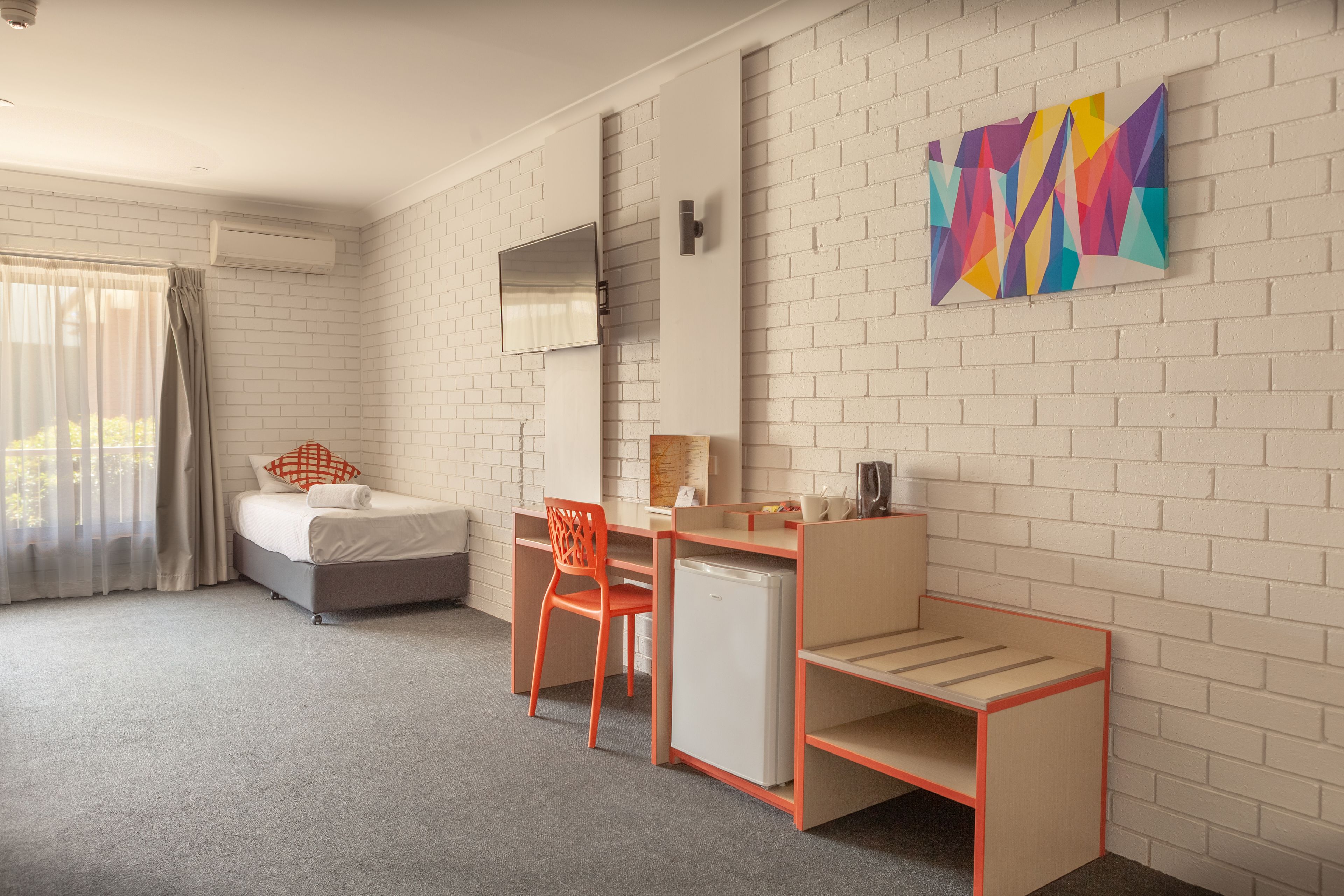 Une chambre d’hôtel équipée d’un lit, d’un bureau, d’une chaise et d’un petit réfrigérateur.