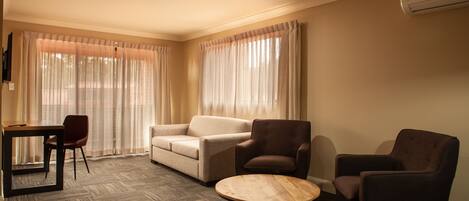 A hotel room with a sofa, two armchairs, a small table, and a TV on the wall.
