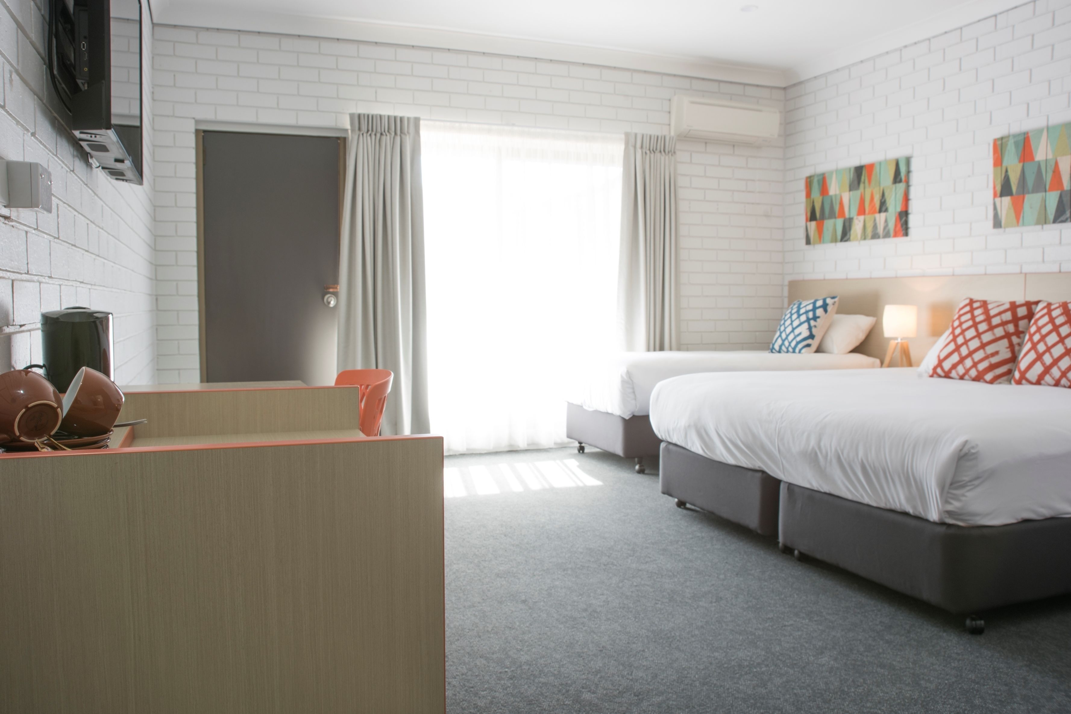 A hotel room with a bed, a desk, a chair, and a window with curtains.