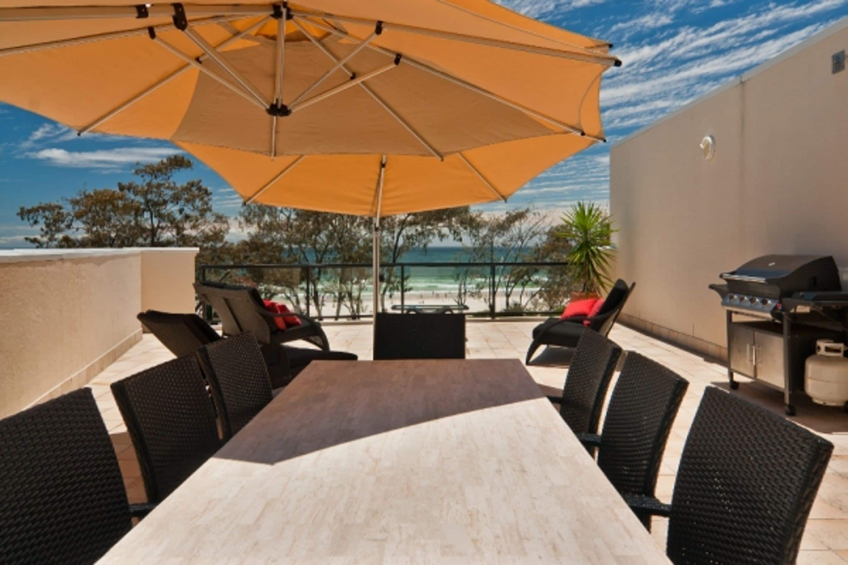 An outdoor patio with a table and chairs, a grill, and a view of the ocean.