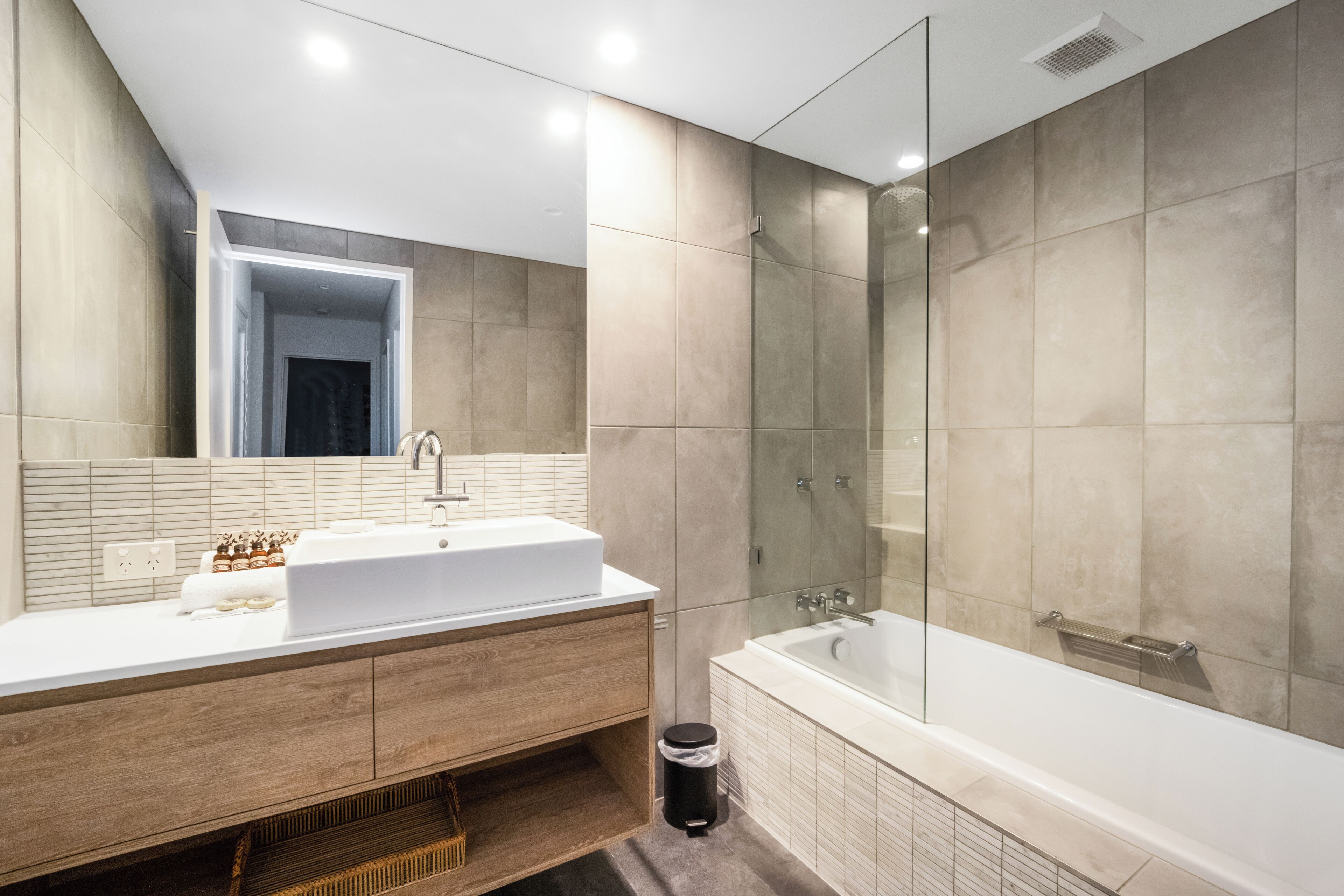 A modern bathroom with a large white bathtub, a wooden vanity with a sink, and a glass shower enclosure.