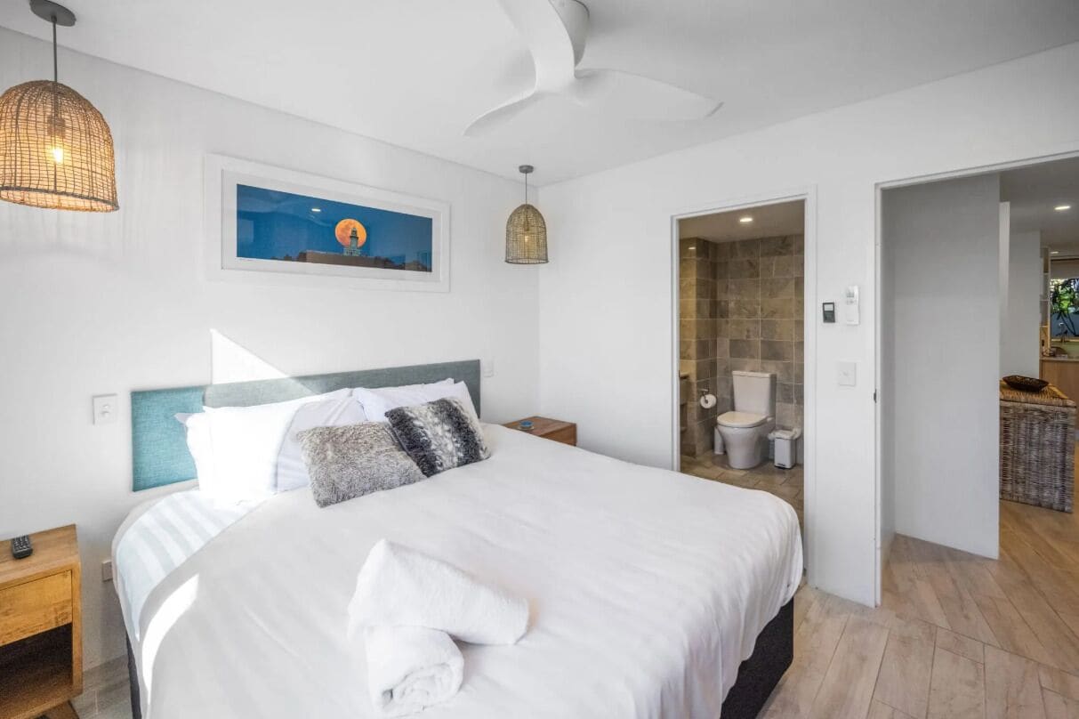 A hotel room with a large bed, a ceiling fan, a framed picture on the wall, and a bathroom visible through an open door.