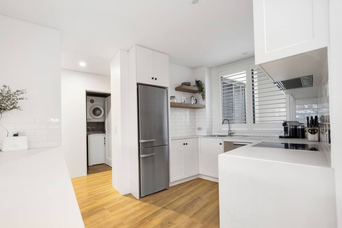 A modern kitchen with white cabinetry, a stainless steel refrigerator, and a wooden floor.