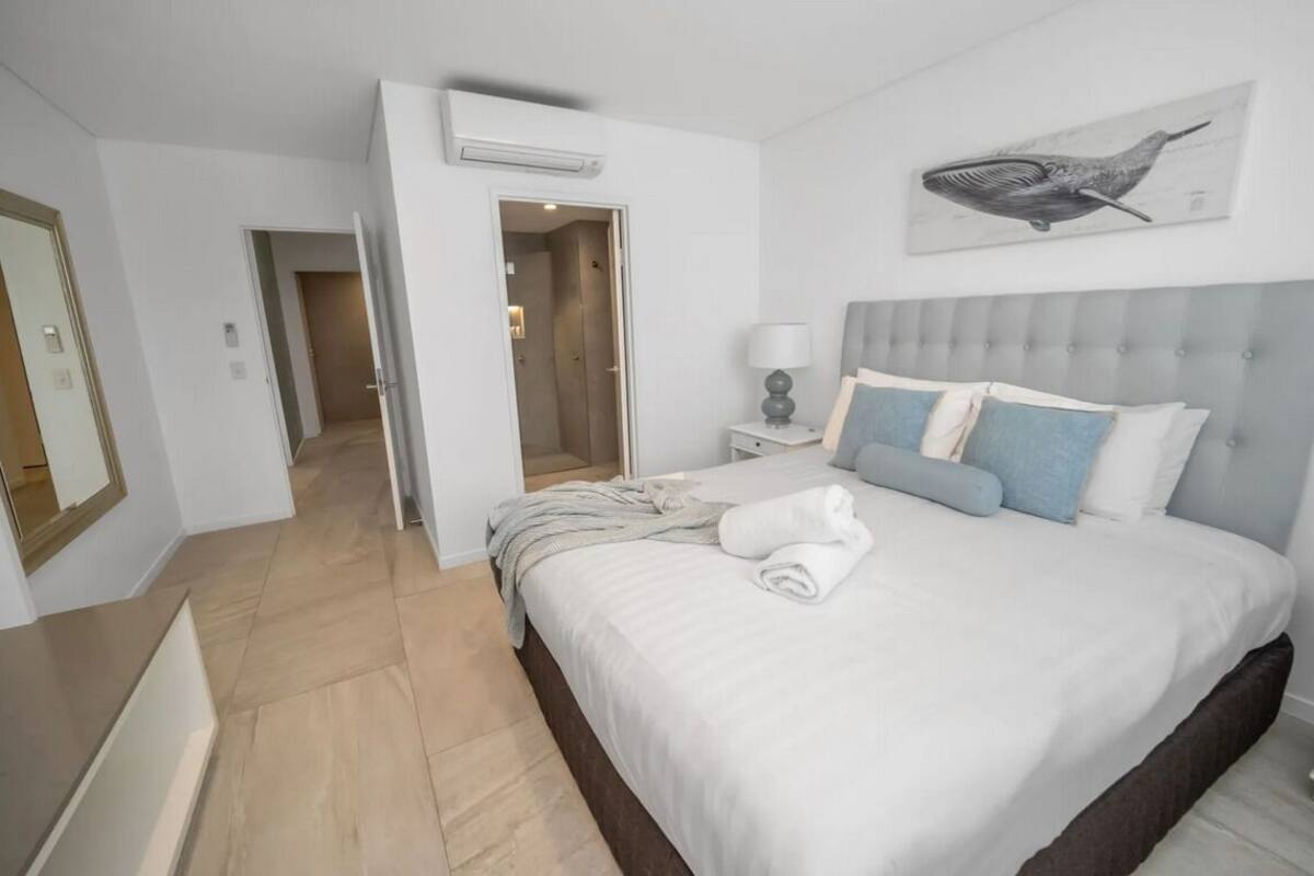 A hotel room with a bed, a nightstand, a lamp, a painting, and a door leading to another room.