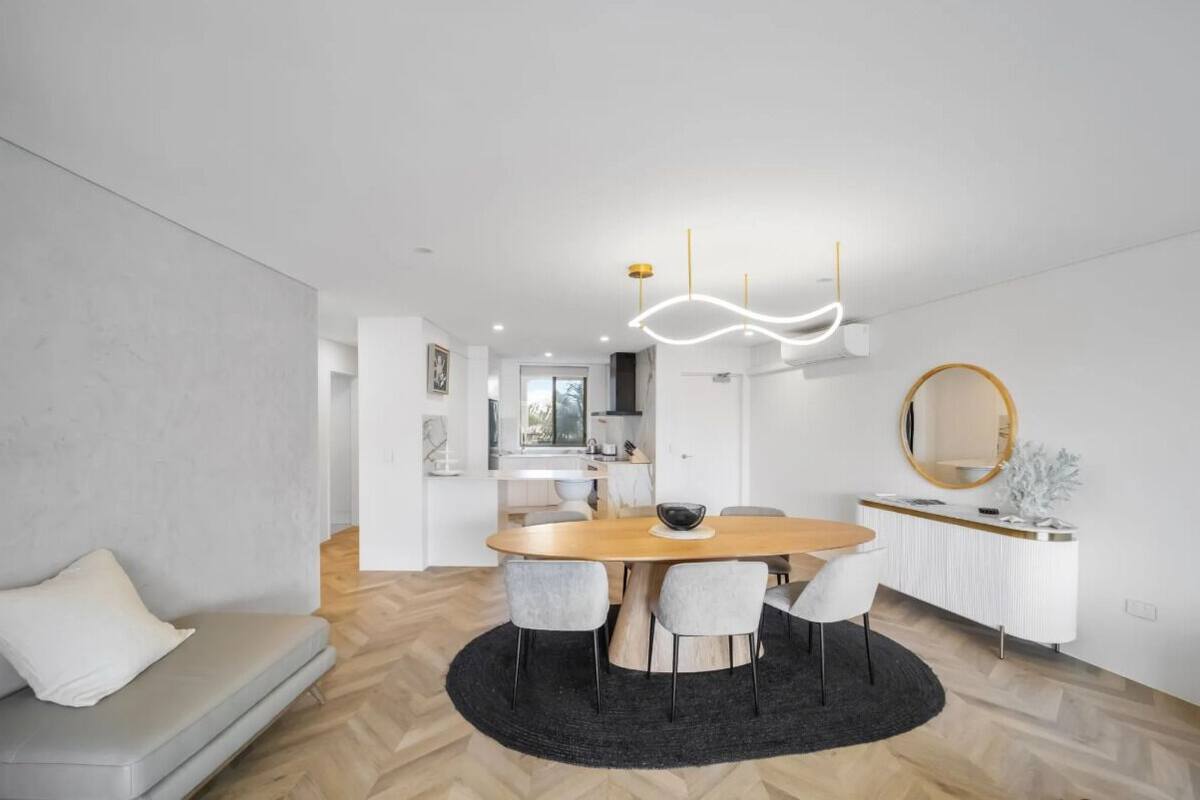 A modern dining area with a round table, grey chairs, and a black rug.