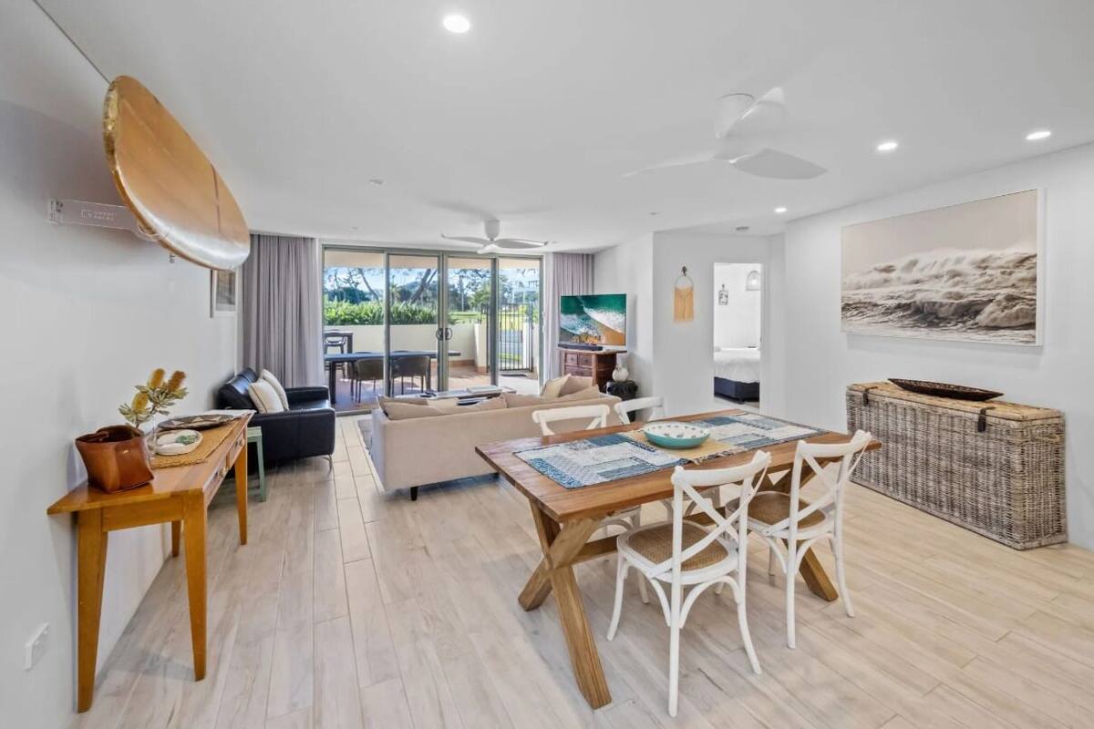 A spacious living area with a dining table, sofas, and a large window overlooking a garden.