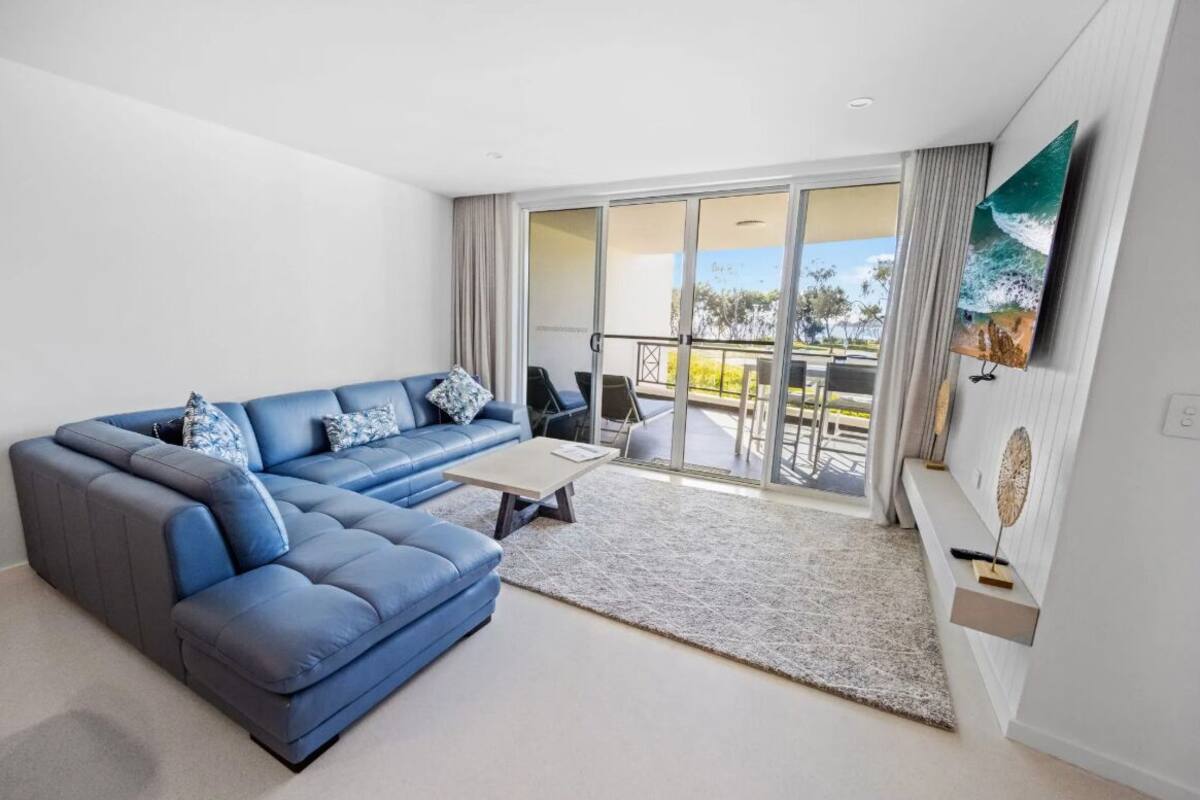 A modern living room with a blue sectional sofa, a small coffee table, and a view of the outdoor balcony.