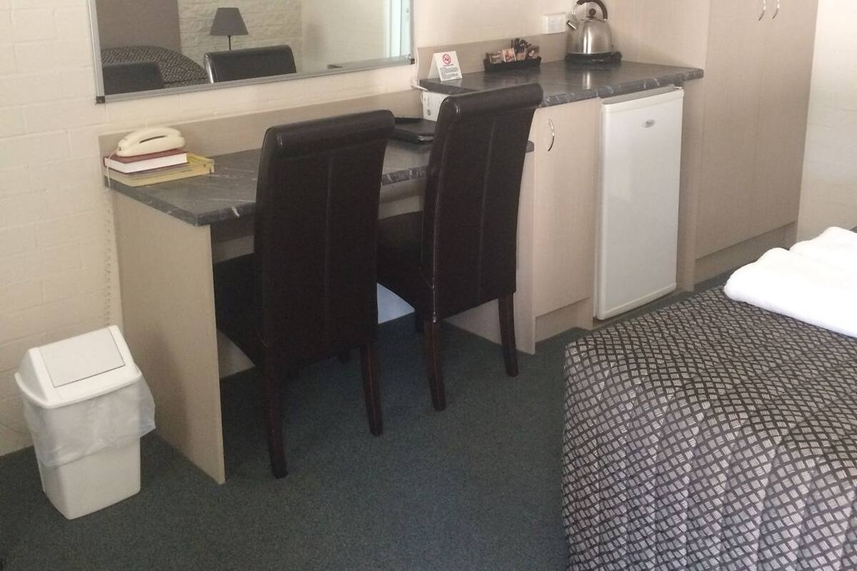 A hotel room with a desk, chair, TV, bed, and a small kitchenette.