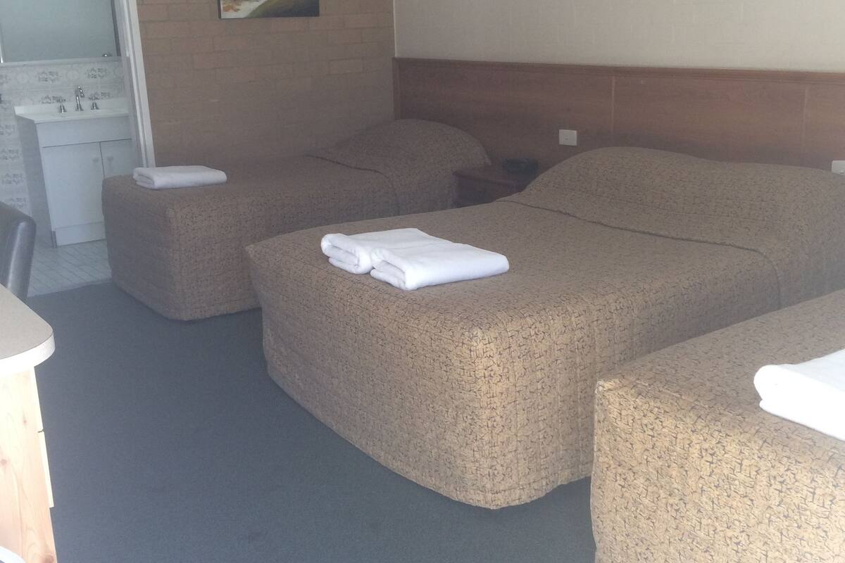 A hotel room with a large bed, two smaller beds, a desk, and a bathroom.