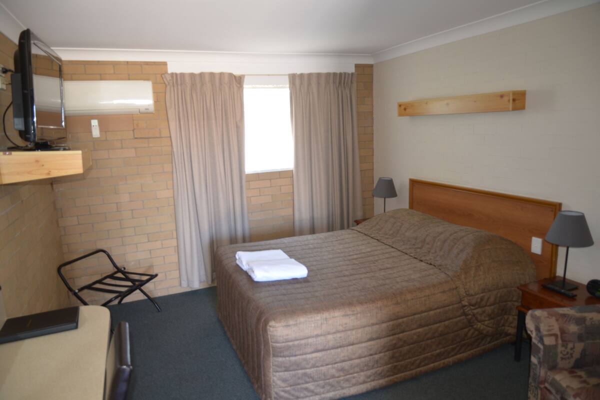 A hotel room with a bed, a TV, a chair, a desk, and a window with curtains.