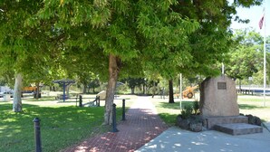 A paved pathway in a park with a stone monument, benches, and trees.