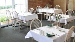 A dining area with tables and chairs, a brick wall, and a window with an 'EXIT' sign.
