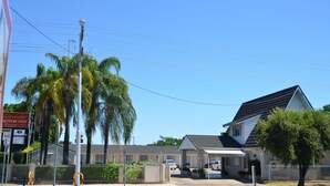 A motel with a row of rooms, a covered parking area, and a palm tree in the foreground.