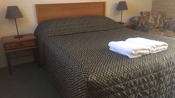 A neatly made bed with a quilted cover, two bedside lamps, and a small wooden nightstand with a drawer.