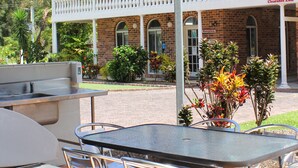 An outdoor patio with a table and chairs, a barbecue grill, and a building with a balcony in the background. - Aston Motel Yamba (Yamba)