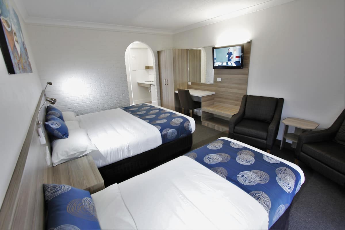Habitación de hotel con dos camas, un escritorio, una silla y un televisor.