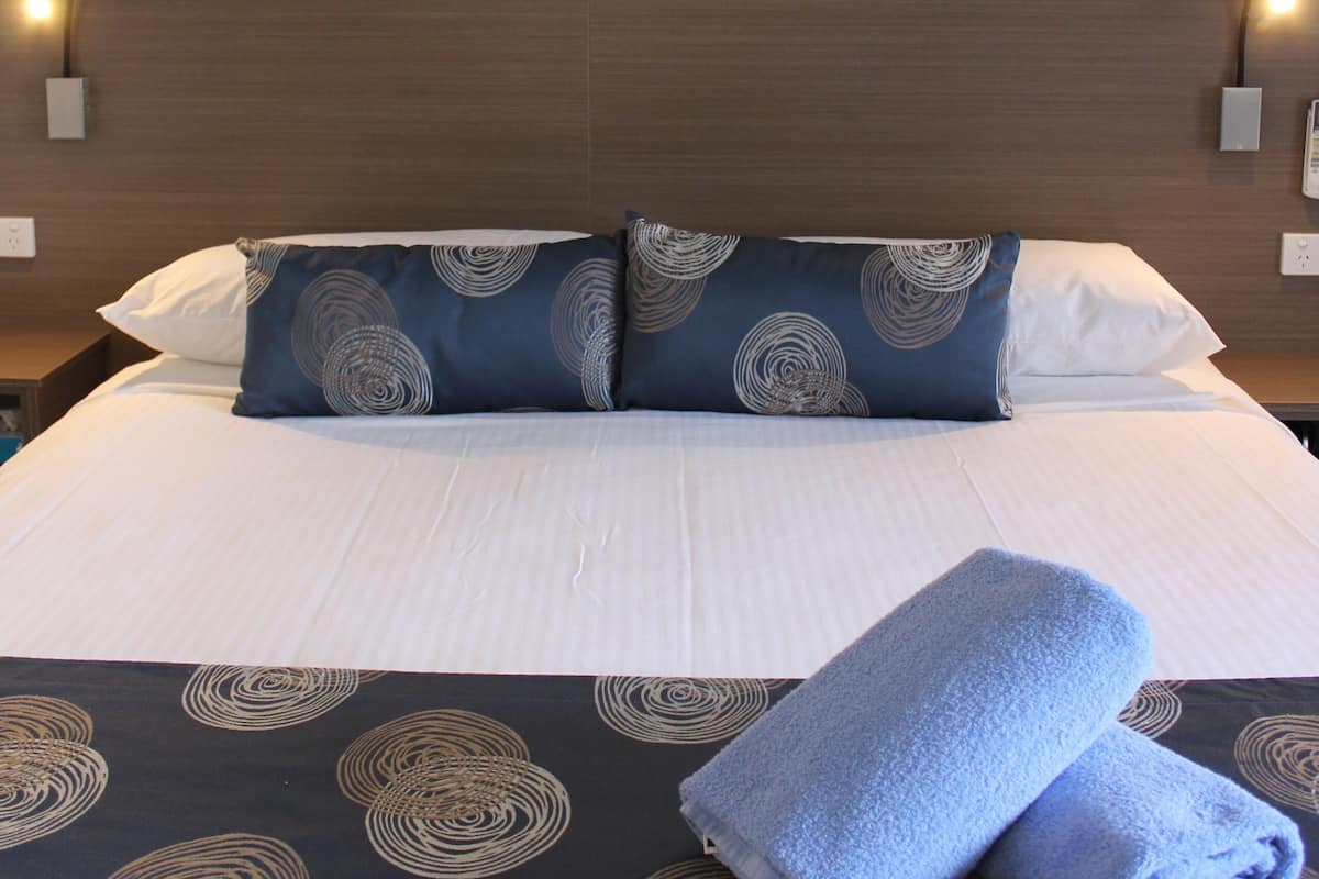 Una cama bien hecha con ropa de cama estampada, un cuadro en la pared superior y dos lámparas de noche.