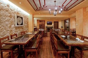A restaurant with wooden tables and chairs, stone walls, and a chandelier. - Kassaros (Metsovo)