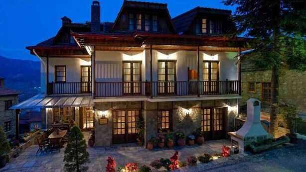 Un edificio de dos pisos con balcón, fachada de piedra y zona de estar al aire libre.