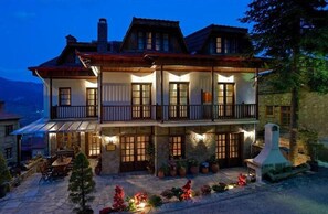 A two-story building with a balcony, stone facade, and outdoor seating area. - Kassaros (Metsovo)