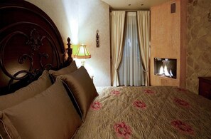 A bedroom with a bed, pillows, a lamp, a window with curtains, and a fireplace. - Kassaros (Metsovo)