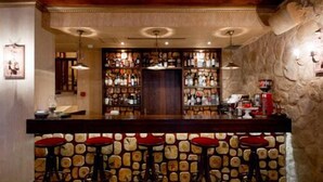 Zona de bar con pared de piedra de fondo, varios taburetes y una variedad de botellas en estanterías.
