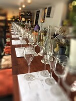 Ett långt bord med flera vinglas och vinflaskor, troligen i en bar eller restaurang.