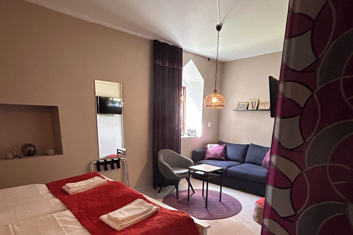 A hotel room with a bed, a desk, a chair, a sofa, and a hanging light fixture.