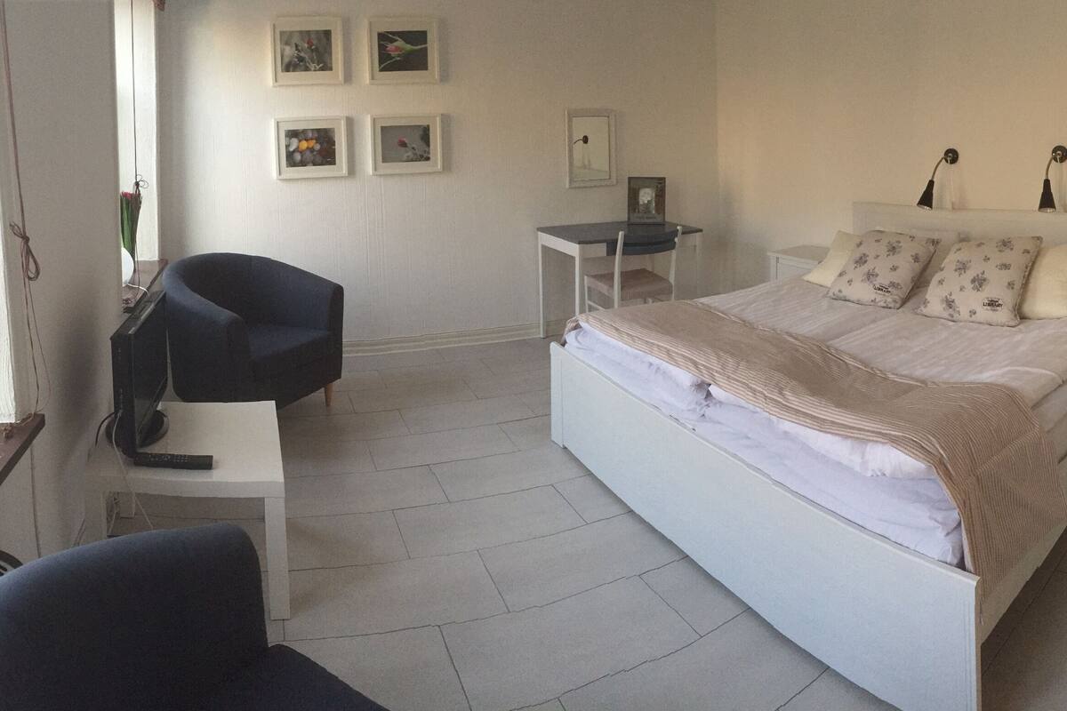 A bedroom with a bed, a desk, a chair, and a small table.