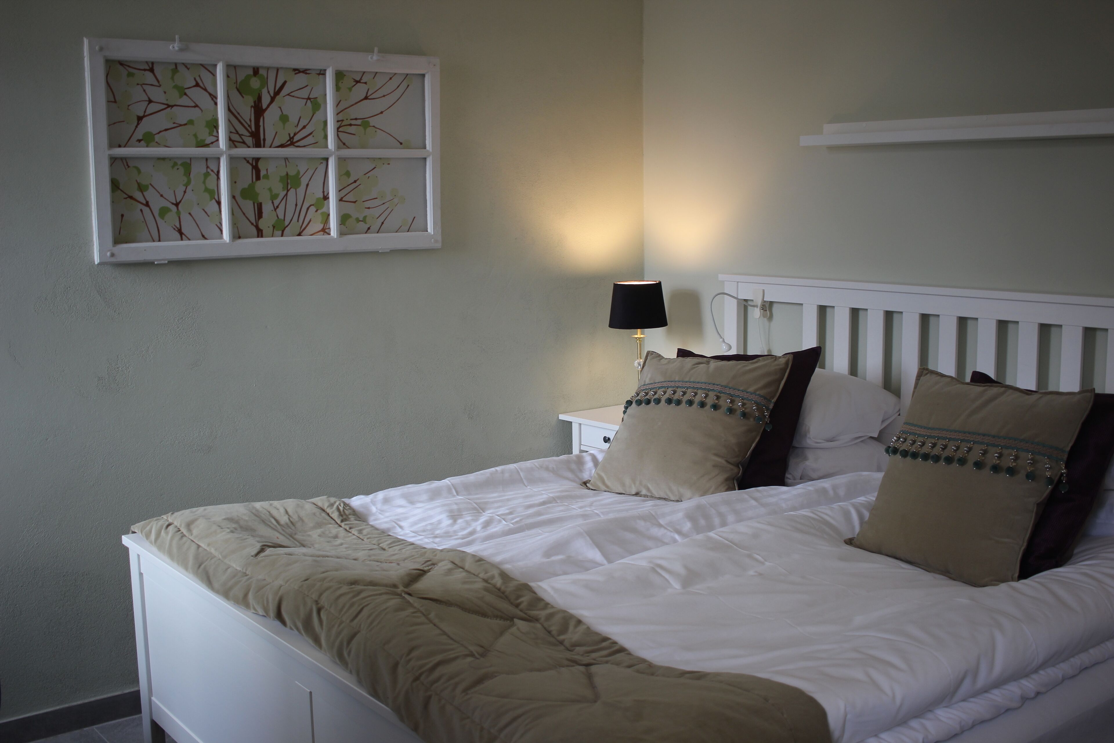 A neatly made bed with a white headboard, a bedside table with a lamp, and a window with a tree design.