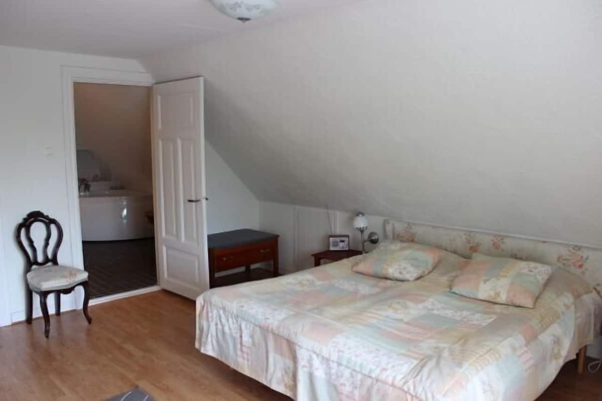 A bedroom with a bed, a chair, a nightstand, and a door leading to another room.