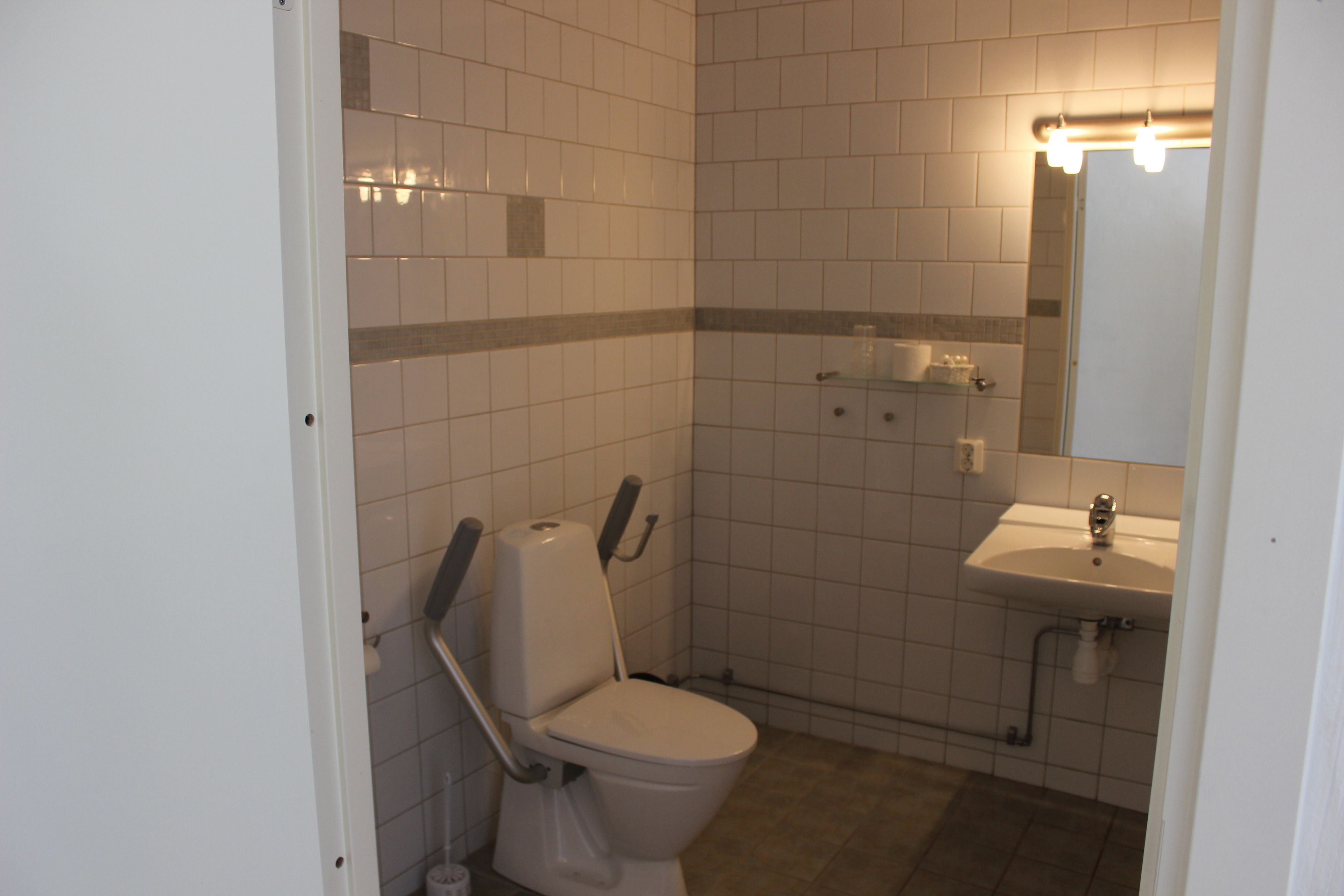 A small, clean bathroom with white tiles, a toilet, a sink, and a mirror.