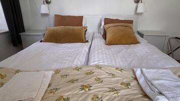 A double bed with floral bedding, two bedside tables, a nightstand, and a shelf with framed pictures.