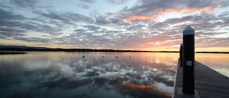 A calm waterfront at sunset with a wooden dock extending into the water.