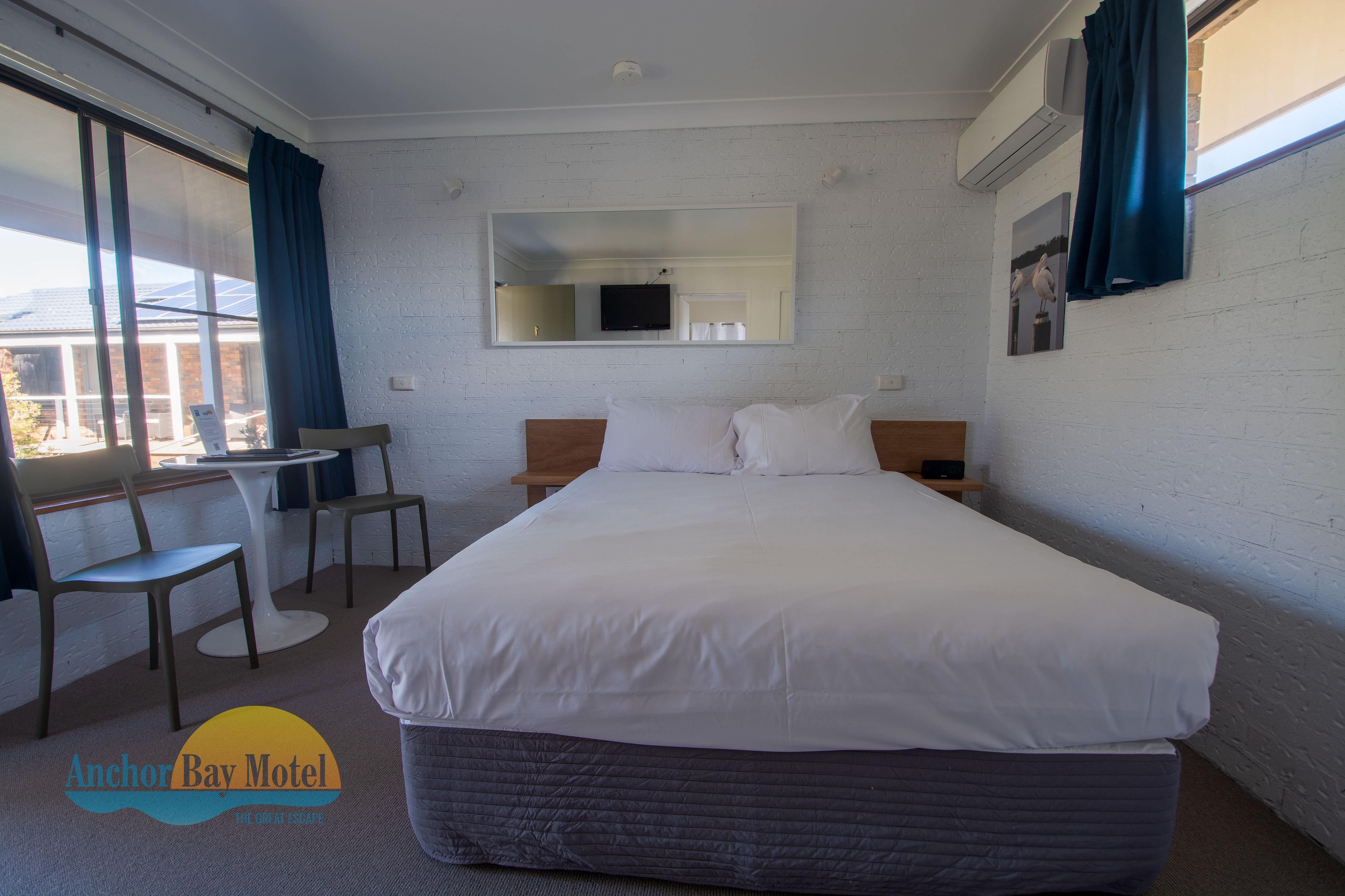 A hotel room with a large bed, a desk, two chairs, a TV, and a window with curtains.