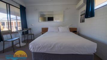 Habitación de hotel con una cama grande, un escritorio, dos sillas, un televisor y una ventana con cortinas.